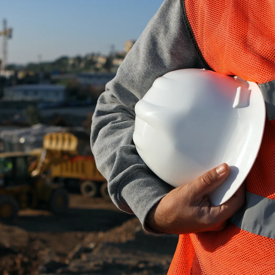 Un ouvrier en gilet orange tenant son casque de chantier sous le bras